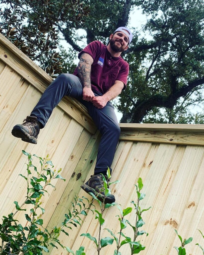 A fencing contractor sitting on a newly installed wooden privacy fence by Heavenly Gates Construction LLC in Miami, FL