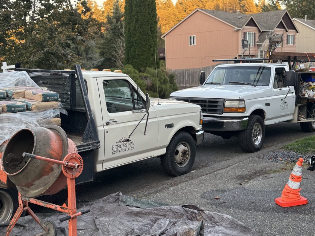 Fences NW LLC work trucks with a concrete mixer and materials on a job site in Spanaway, WA