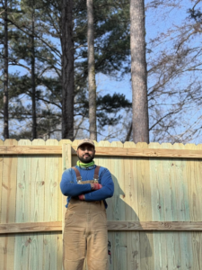 A fencing contractor standing proudly in front of a newly installed wood picket fence by Mayan Fence & Outdoor LLC in Phoenix, AZ.