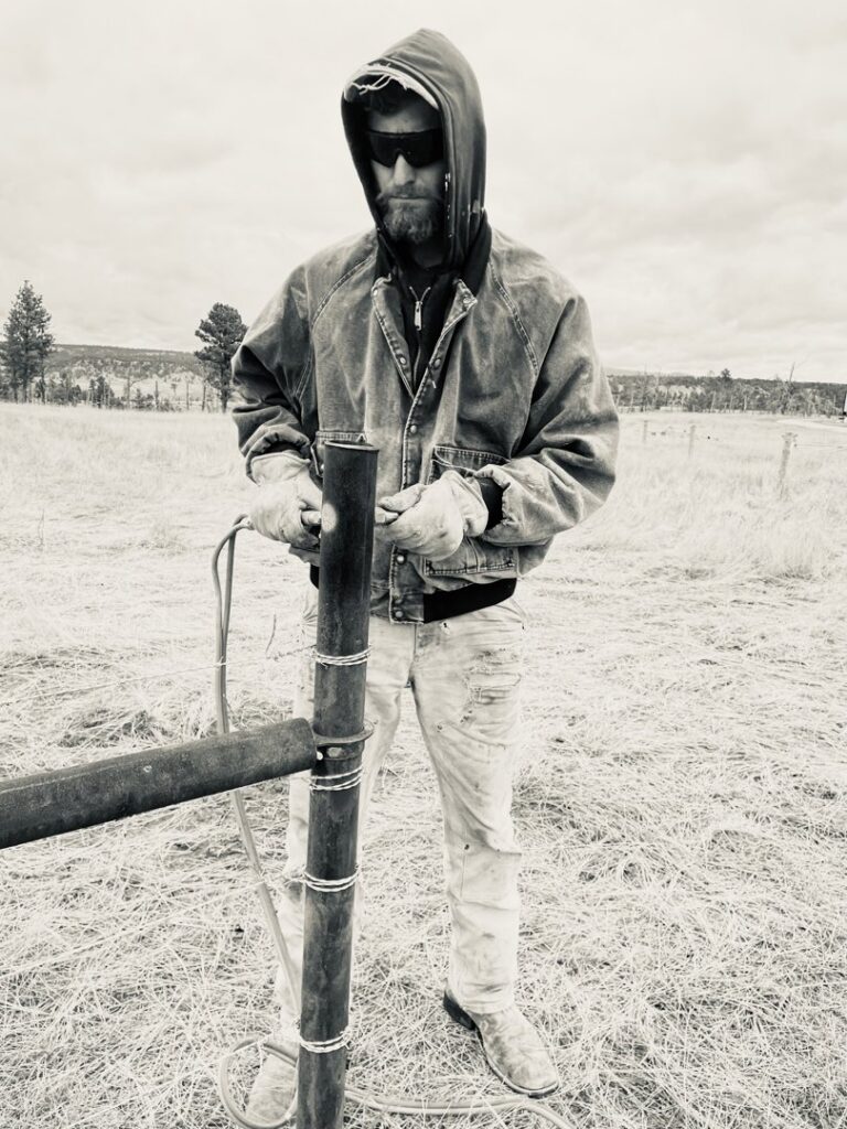 A fencing contractor working on a fence post in a field, representing Cool Hand Fencing and Wyo War Wagons in Laramie, WY.