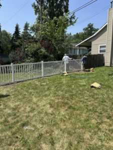 Fencing contractors installing a white picket-style fence in a residential backyard for T & A Fencing in Warren, MI.