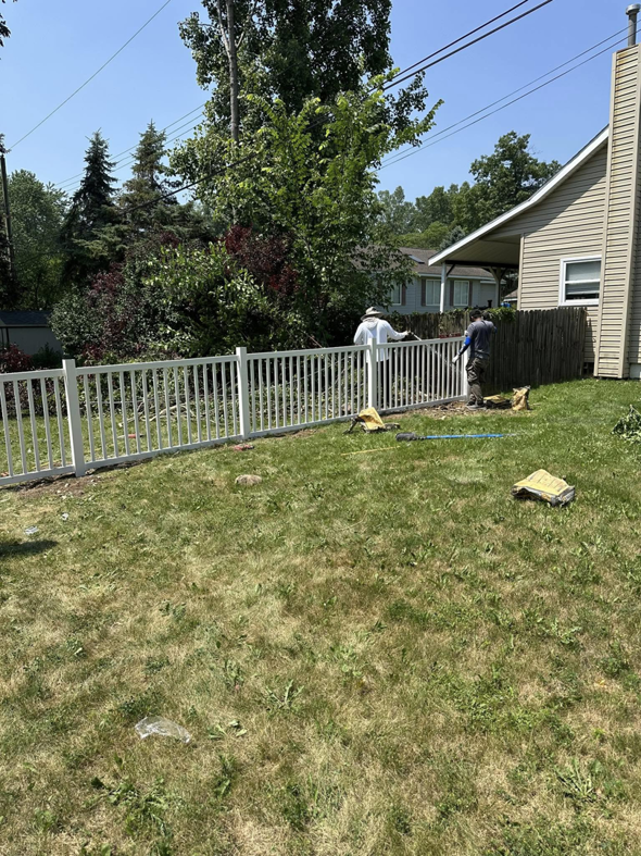 Fencing contractors installing a white picket-style fence in a residential backyard for T & A Fencing in Warren, MI.