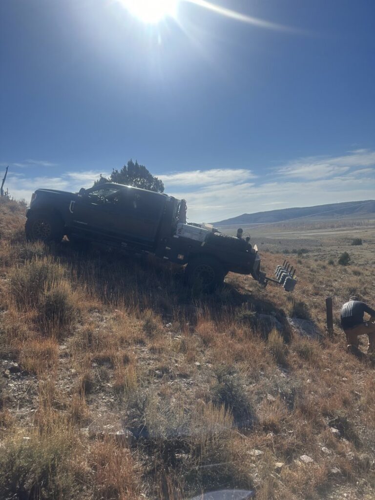 A fencing crew working on a hillside with a work truck carrying fencing materials, by Cool Hand Fencing and Wyo War Wagons in Laramie, WY.