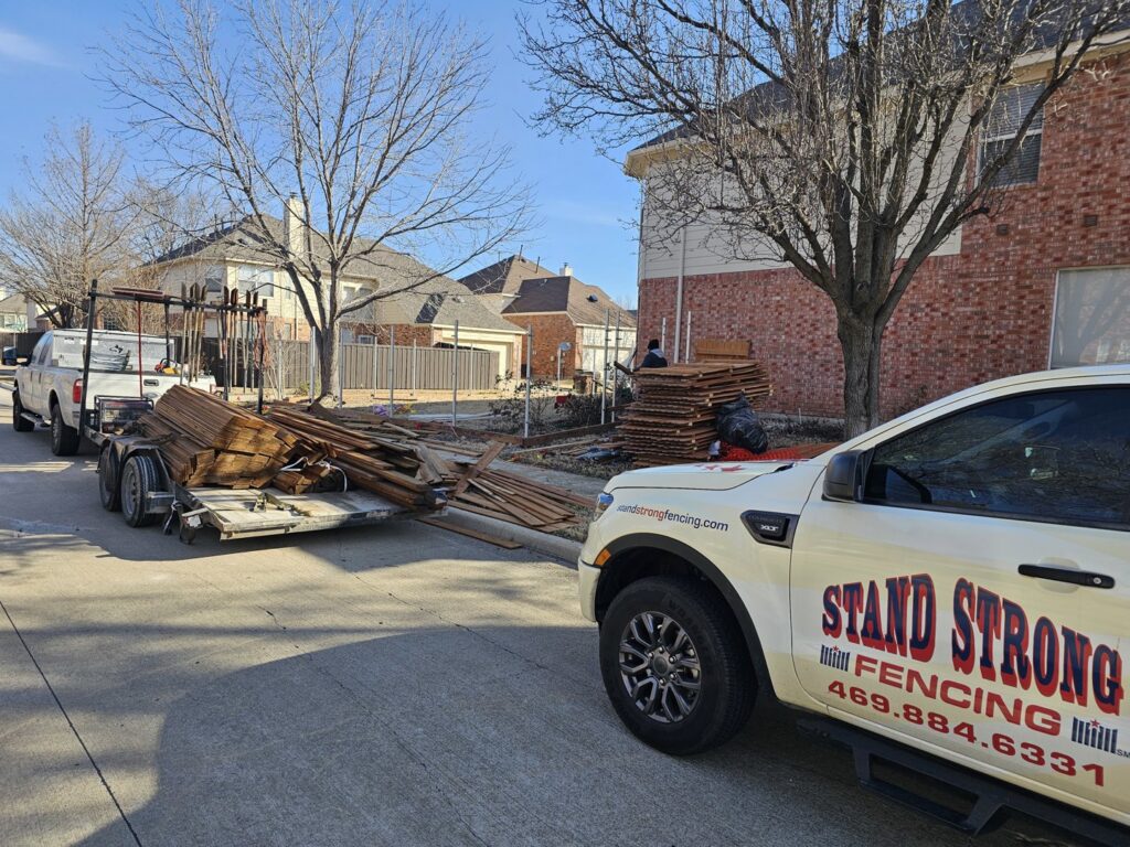 A fencing job site with a Stand Strong Fencing of Plano, TX truck, trailer, and new materials ready for installation
