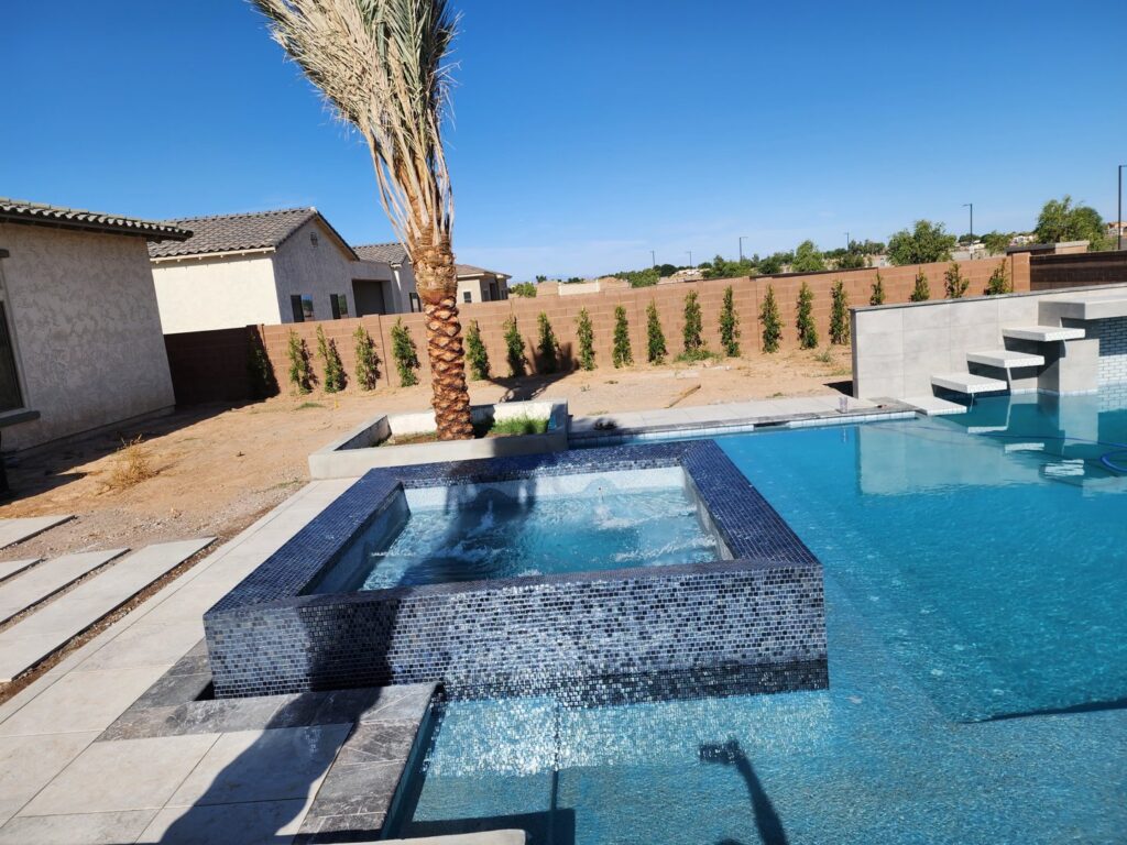 A finished pool with a raised spa, dark tile, and a palm tree in the backyard by EZ POOL Solutions in Tucson, AZ