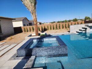 A finished pool with a raised spa, dark tile, and a palm tree in the backyard by EZ POOL Solutions in Tucson, AZ