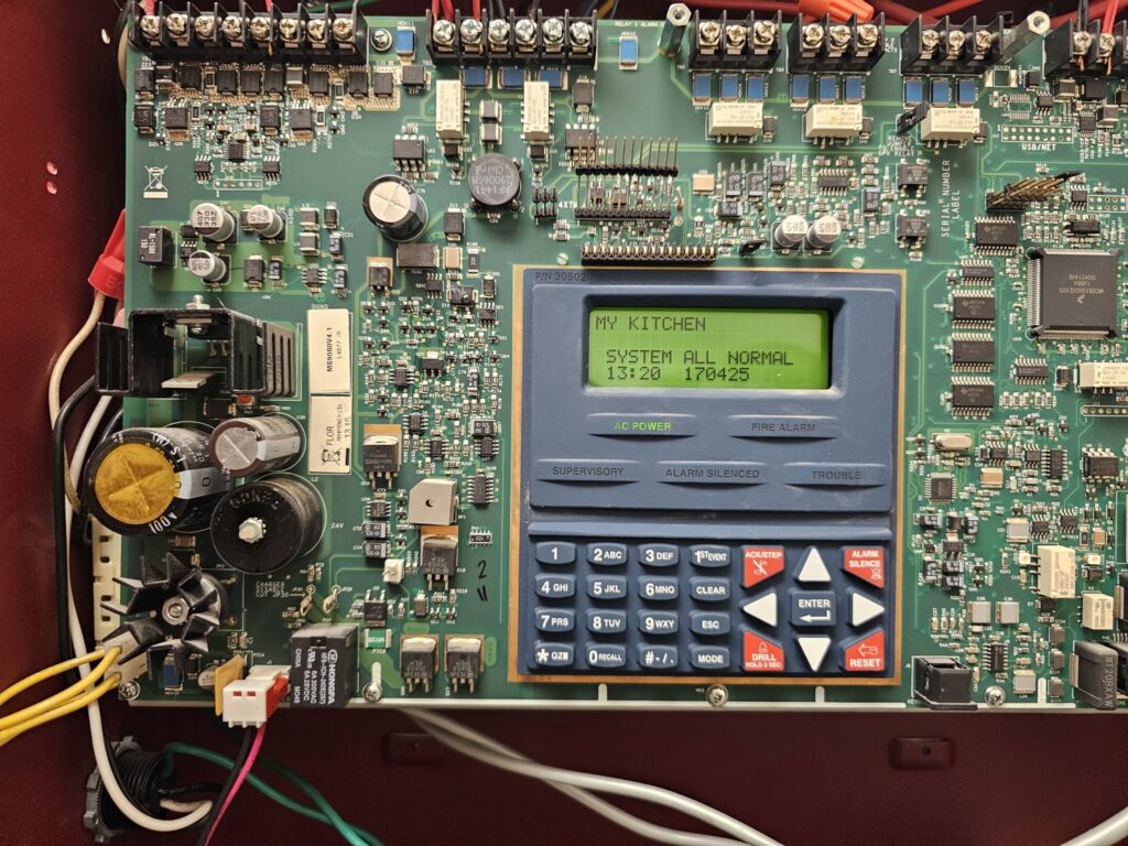 An open fire alarm control panel showing circuit boards and wiring, serviced by Tesla Alarm and Electrical in Plano, TX