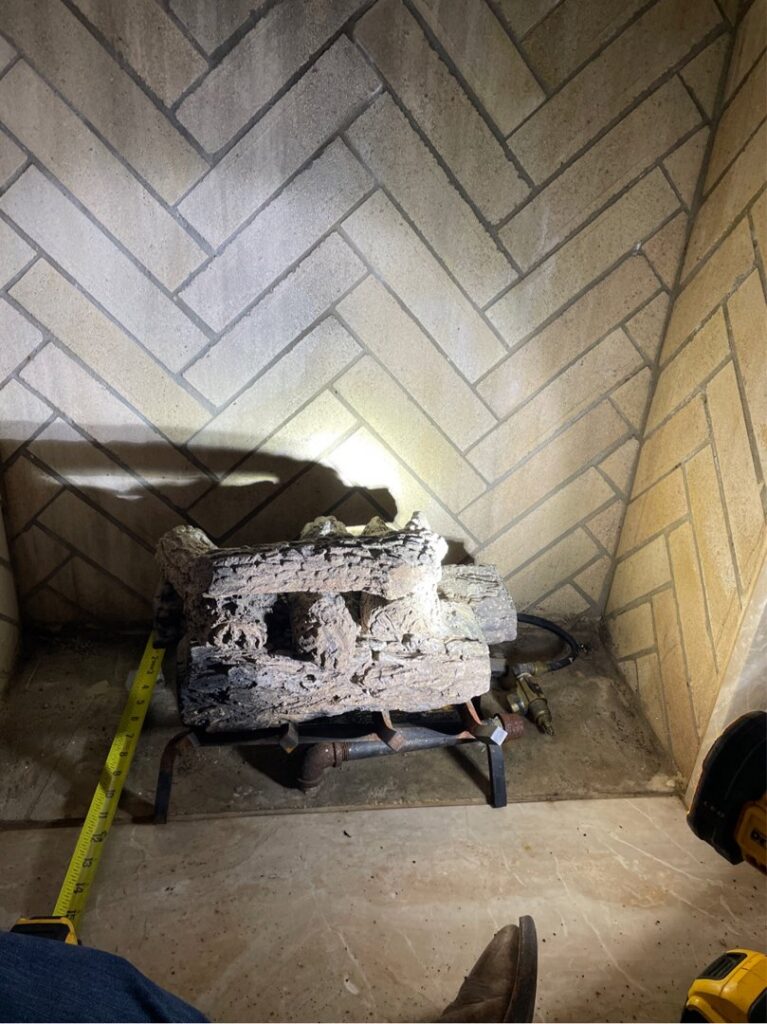 A fireplace inspection in progress, showing gas logs and a measuring tape, by HBR Hearth and Chimney in Dallas, TX