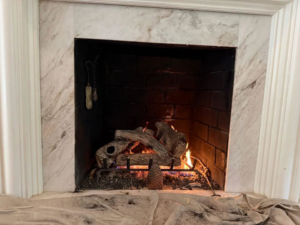 A fireplace interior with gas logs and a drop cloth showing soot, indicating a chimney sweep job by Chimney Care experts in Doraville, GA.
