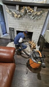 An 832 Home Service technician vacuuming the interior of a fireplace during a chimney sweep in Houston, TX.