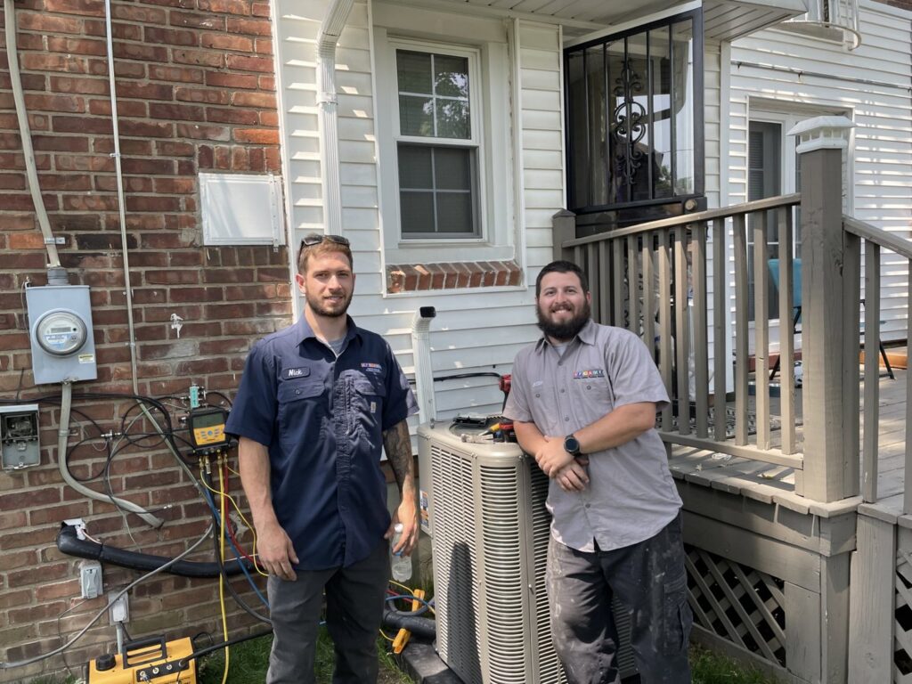 FLAME Heating, Cooling, Plumbing & Electrical technicians servicing an outdoor AC unit with gauges in Warren, MI.