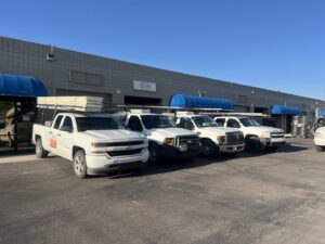 A fleet of 4 Sons Garage Door service trucks, some carrying garage door panels, parked in Phoenix, AZ.