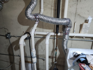 Flexible dryer vent ducts and plumbing in a laundry area, showcasing services by Pro Power Air Duct & Dryer Vent Cleaning in Kenosha, WI.