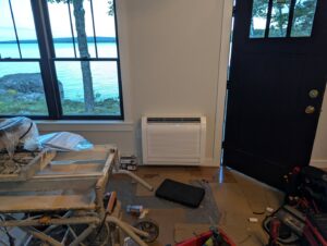 A floor-mounted heat pump unit installed in a room with tools, indicating work by Kinney Family Heat Pumps in Augusta, ME.