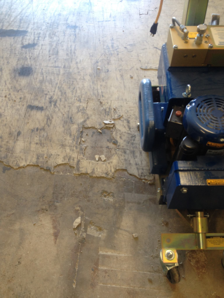A floor removal machine on a concrete floor, showing debris from a removal job by Clean Site Flooring Removal in Sacramento, CA.