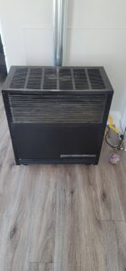 A floor-standing furnace or heater unit with a vent pipe installed in a residential space by Northern Peak Heating & Cooling in Bozeman, MT.