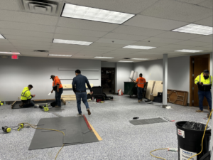 Workers installing new flooring, likely carpet tiles, in a large commercial space by Hank's Specialties, Inc. in Saint Paul, MN.