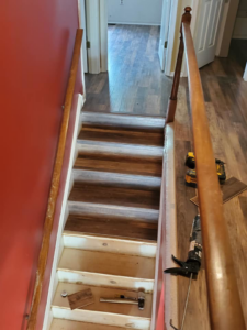 Flooring installation in progress on a staircase, showing new wood-look planks being laid by TJS Floorcovering in Pennsauken, NJ.