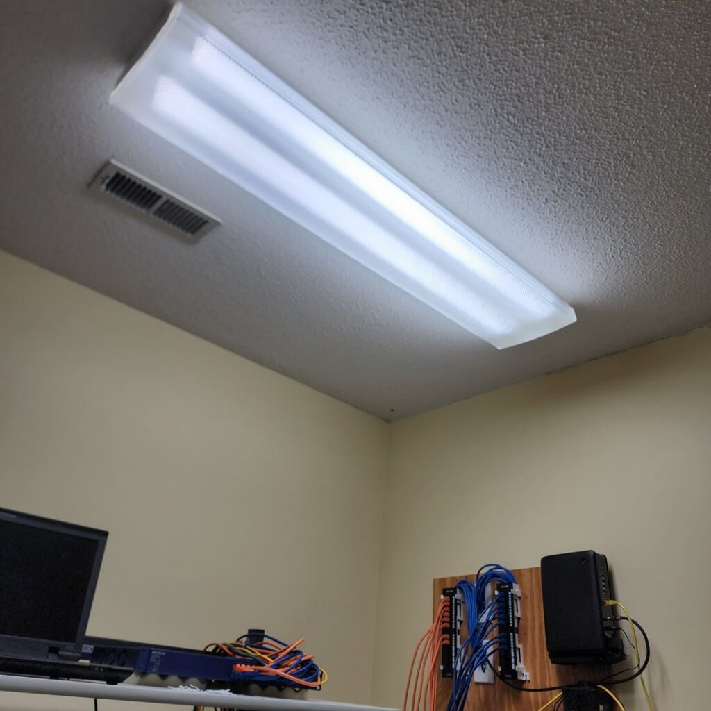 A newly installed fluorescent light fixture and organized network cabling on a wooden board by True Vine Electric in Raleigh, NC