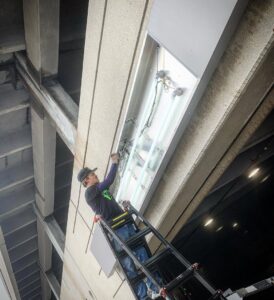 An electrician from Lumenus Technologies, LLC repairing a fluorescent light fixture in Lenexa, KS.