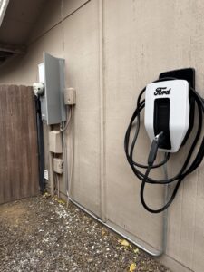 A Ford electric vehicle charger installed on an exterior wall next to an electrical panel by Castle Electrical & Lighting in Scottsdale, AZ.