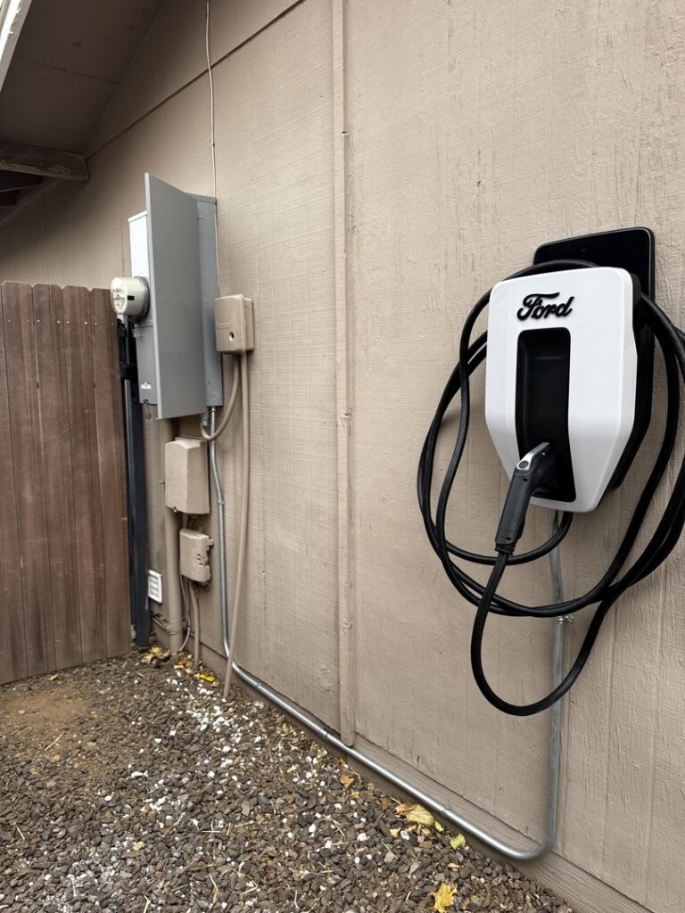 A Ford electric vehicle charger installed on an exterior wall next to an electrical panel by Castle Electrical & Lighting in Scottsdale, AZ.