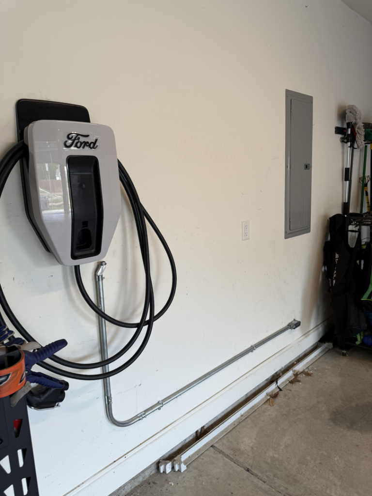 A Ford EV charger installed on a garage wall next to an electrical panel by Jackson Electrical Service LLC in Birmingham, AL