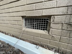 A foundation vent with a metal grate, a common pest entry point, inspected by The Squirrel Guys in Birmingham, AL.