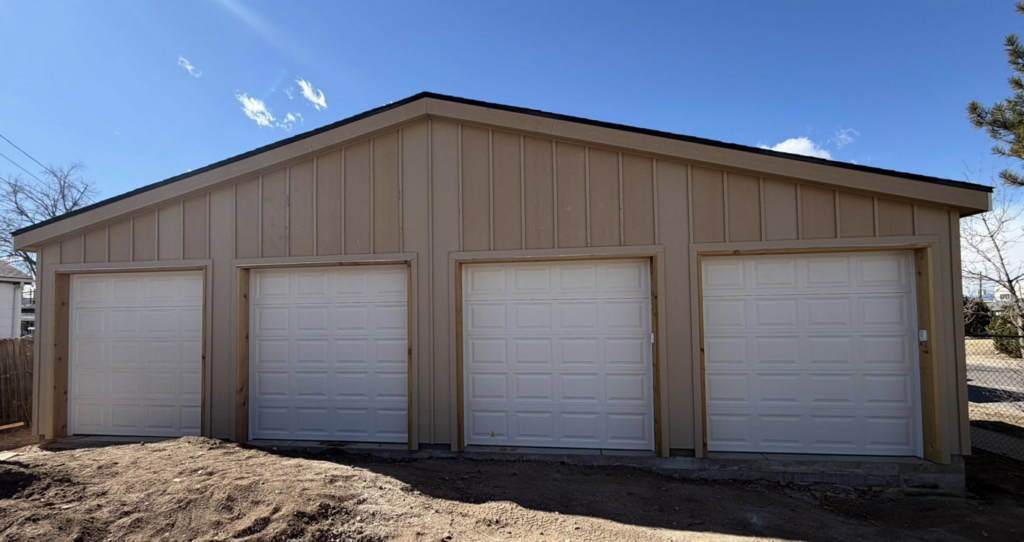 Four newly installed white panel garage doors on a tan commercial or residential building by 365GarageDoor in Dallas, TX