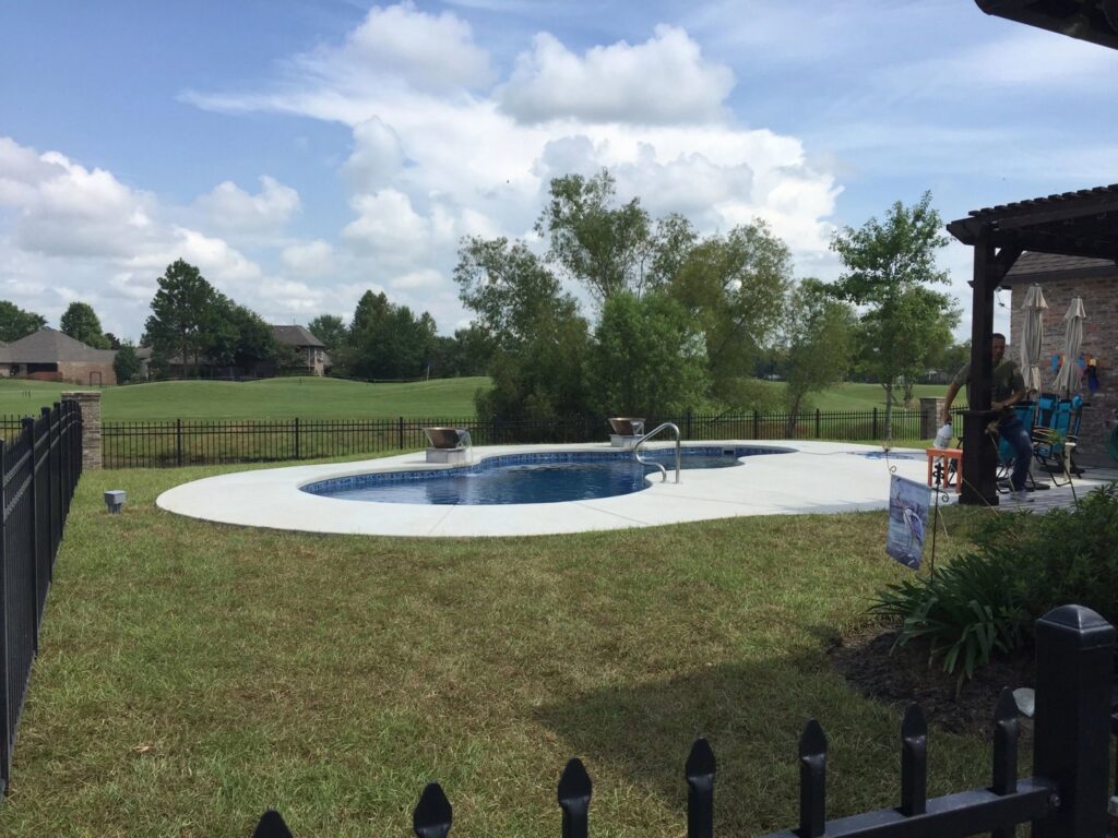 A freeform swimming pool with a fence, situated next to a golf course by Central Pools, Inc. in Baton Rouge, LA