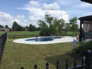 A freeform swimming pool with a fence, situated next to a golf course by Central Pools, Inc. in Baton Rouge, LA