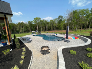 A beautiful freeform pool surrounded by a paver patio and lush landscaping, created by Luxury Outdoors in Murfreesboro, TN.
