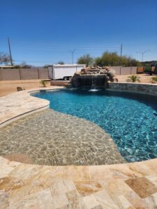 A beautiful freeform pool with a natural rock waterfall and stone decking by EZ POOL Solutions in Tucson, AZ
