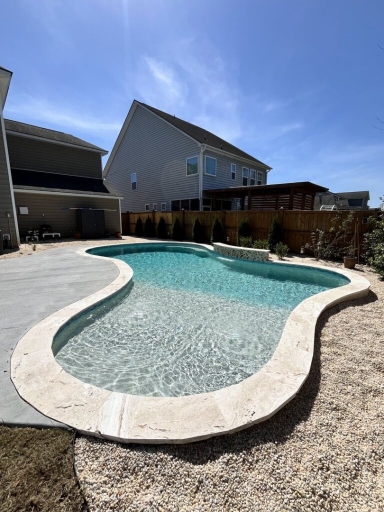 A freeform swimming pool with a decorative water feature and mixed landscaping, completed by Salty Reef Pools LLC in Summerville, SC.