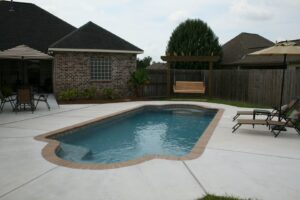 A freeform swimming pool featuring brick coping and a spacious concrete patio by Central Pools, Inc. in Baton Rouge, LA.