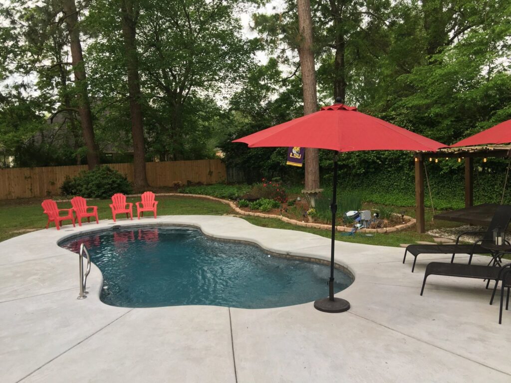A freeform swimming pool with a red umbrella and lounge chairs by Central Pools, Inc. in Baton Rouge, LA