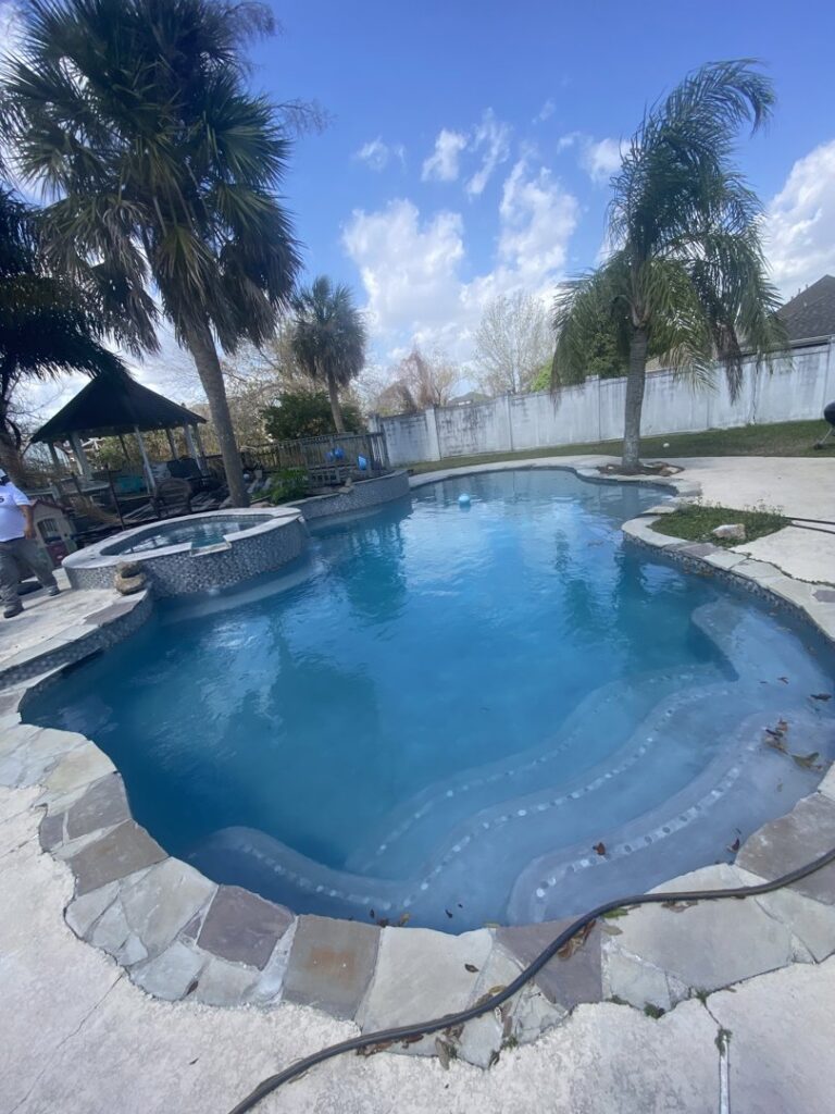 A beautiful freeform swimming pool with natural stone coping and an attached spa, built by I10 Pool Plastering LLC in Kenner, LA.