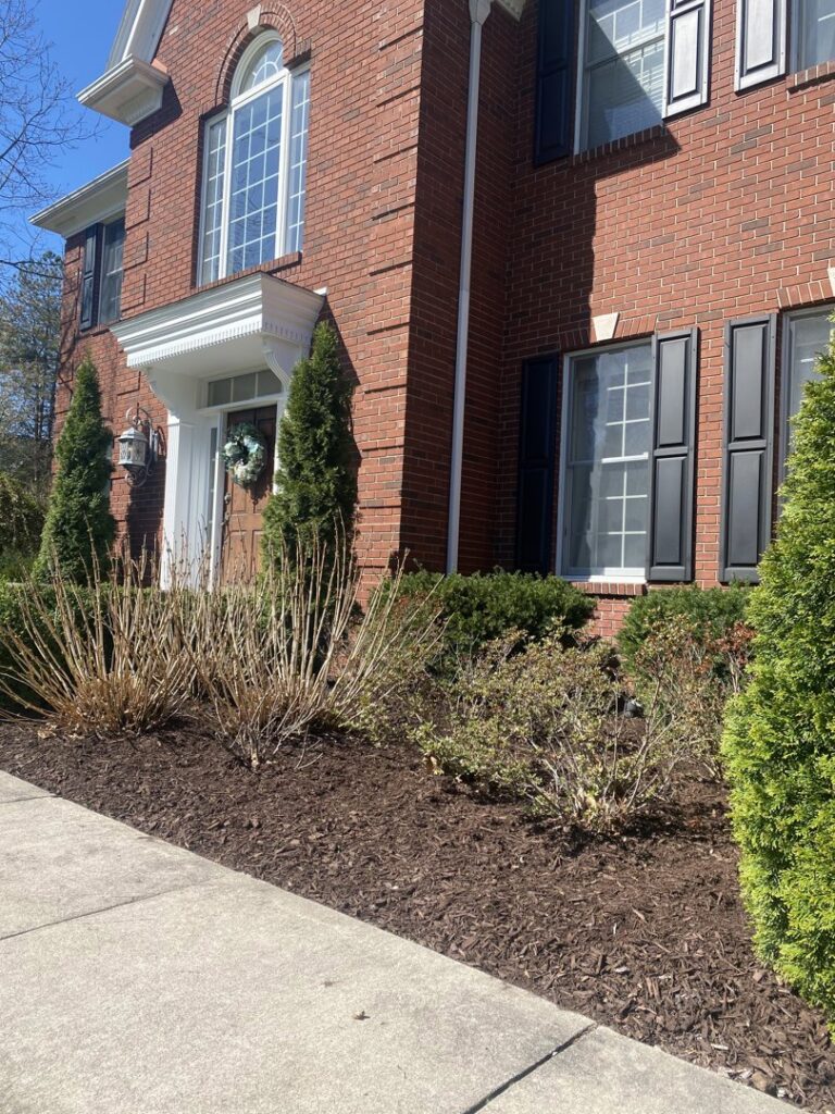 Fresh mulch applied to landscaping beds in front of a brick home, a service by Roots Lawn Care Solutions in Granger, IN.