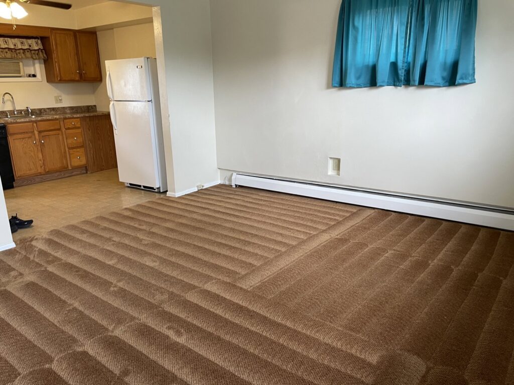 Freshly cleaned brown carpet in a room adjacent to a kitchen, showing cleaning lines from KANDE Carpet Cleaning in Pittsburgh, PA.