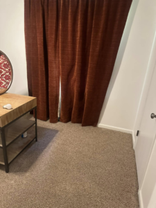 Freshly cleaned carpet in a bedroom with curtains and a small table by The Gold Standard Carpet Cleaning in Kansas City, MO.
