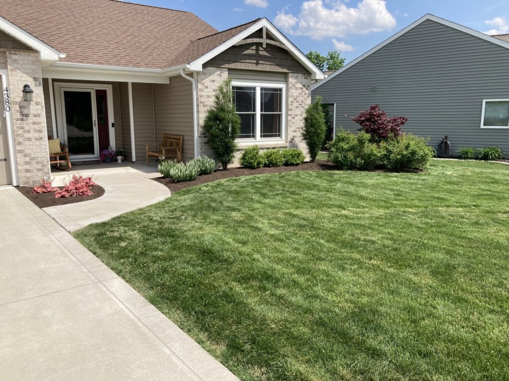 A freshly cut and well-maintained residential lawn with mulched flower beds by Three Rivers Lawn Care Co. in Fort Wayne, IN.