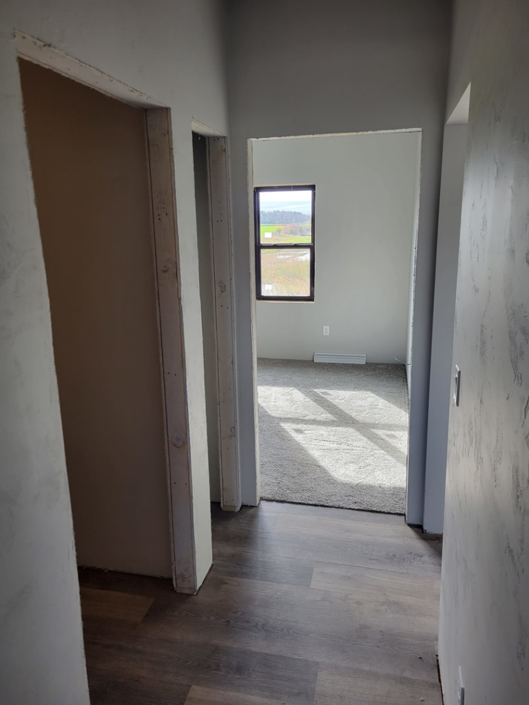 A view into a room with freshly installed carpet, seen from a hallway with wood-look flooring, by SchuhLess Flooring and Remodeling, LLC in Appleton, WI.