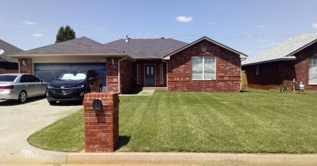 A beautifully mowed front lawn with crisp stripes at a brick house by You're Choice Lawn Care LLC in Oklahoma City, OK.