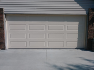 Frontal exterior view of a beige panel garage door installed on a residential property by R&A Overhead Door in Gower, MO.