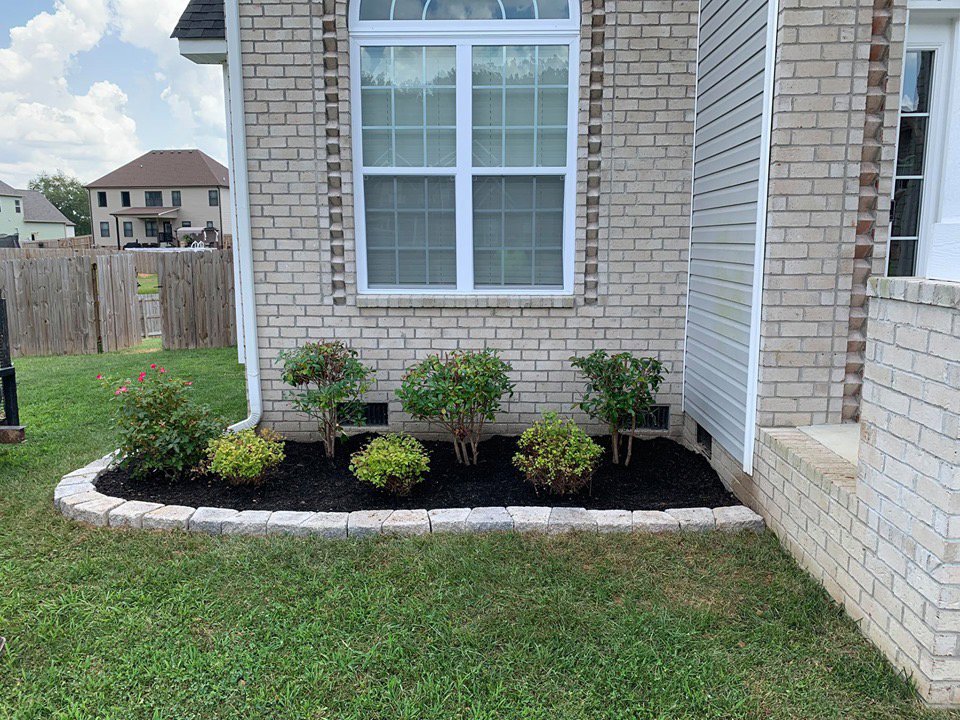 Front yard landscaping with fresh mulch and plants, bordered by pavers, by Cutting Edge Lawn Services in Islip, NY