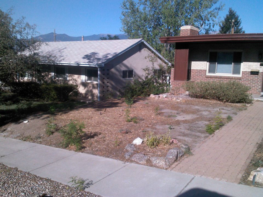 A front yard undergoing landscaping site preparation with cleared ground and fresh mulch by RMMLS in Colorado Springs, CO.