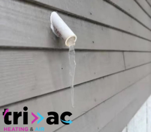 A frozen HVAC condensate drain pipe with ice dripping from a house wall, indicating a potential issue, by TRI AC in Canton, GA.