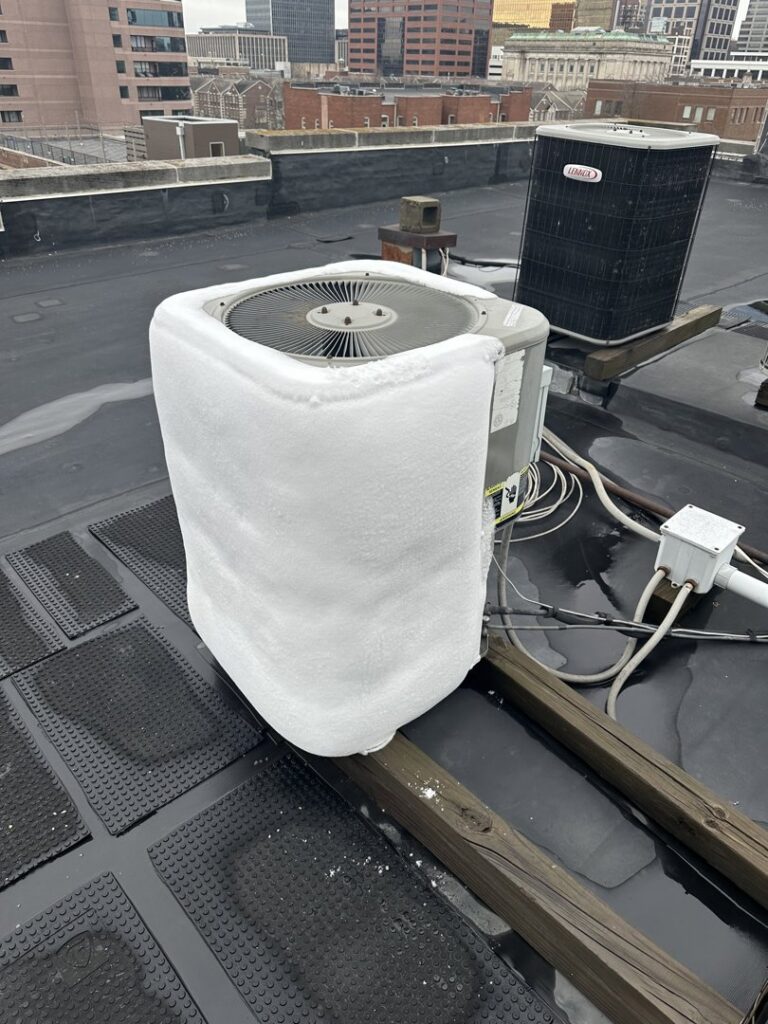 A residential outdoor AC unit covered in snow and ice, requiring winter service from Radiant Heating & Cooling in Fishers, IN.