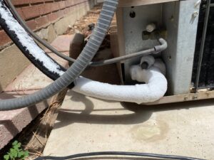 A close-up of a frozen refrigerant line on an outdoor AC unit, indicating a repair job by Hansen HVAC & Plumbing Services, Inc. in West Jordan, UT.