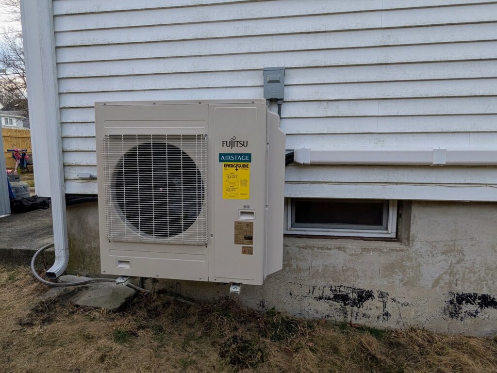A Fujitsu Airstage outdoor HVAC unit installed on the exterior of a home by WARM Global HVAC in East Providence, RI